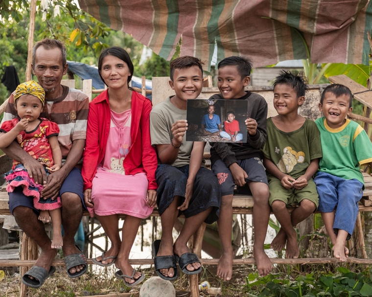 Alim and Rajib smiling with their family and holding a photo of themselves before cleft surgery