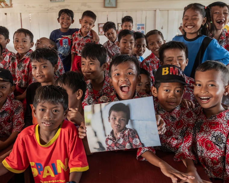 Rajib smiling with his friends and holding a picture of himself before cleft surgery